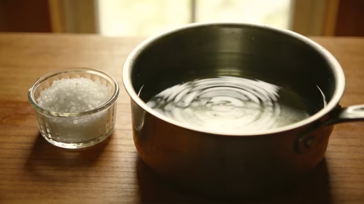 Preparo do banho de sal grosso — panela com água e potinho de sal grosso sobre a mesa