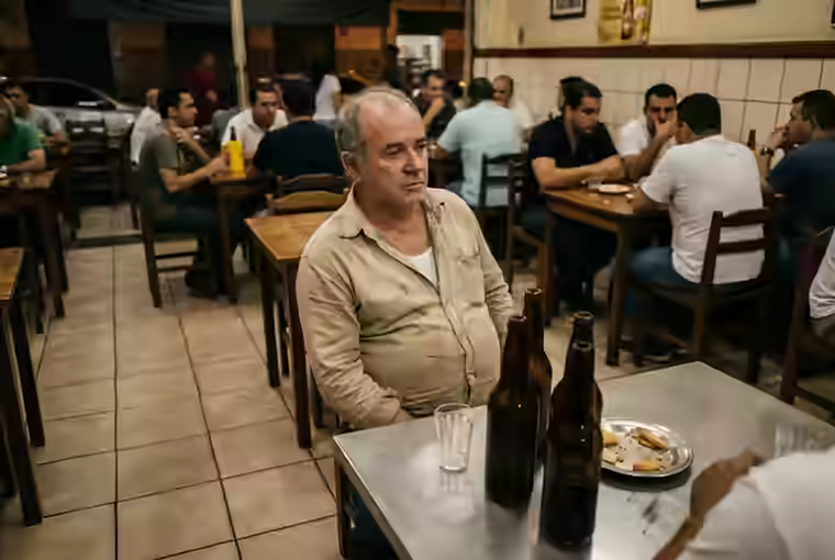 Homem bebendo sozinho a uma mesa de boteco cheio de gente