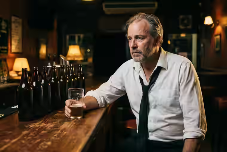 Homem sentado no balcão de um bar com um copo de cerveja na mão